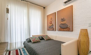 A bedroom with a bed, curtains, a wall-mounted air conditioner, and two paintings. - Apart in Thai Beach Home Spa Cond sea Front Tbs106 (Florianópolis)