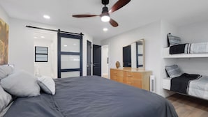 Ein modernes Schlafzimmer mit einem großen Bett, einem Schminktisch, einem Spiegel, einem Deckenventilator und einem Etagenbett.