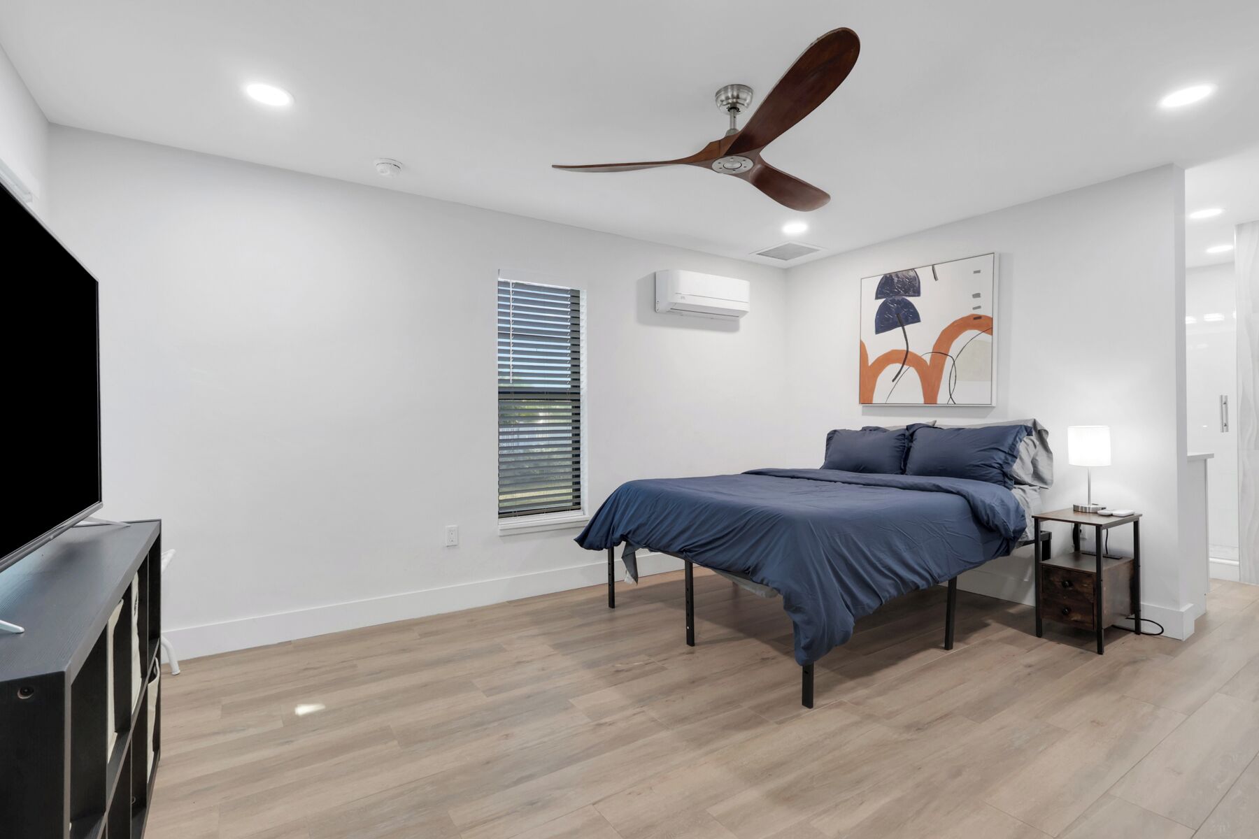 A bedroom with a bed, a ceiling fan, a TV, and a window with blinds.