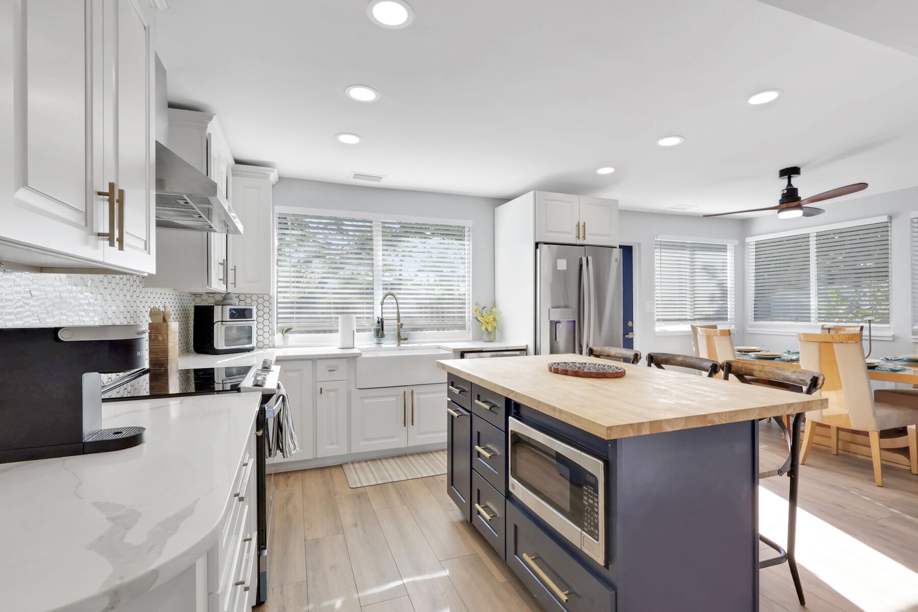 A modern kitchen with white cabinets, a large island, and a dining area with a wooden table and chairs.