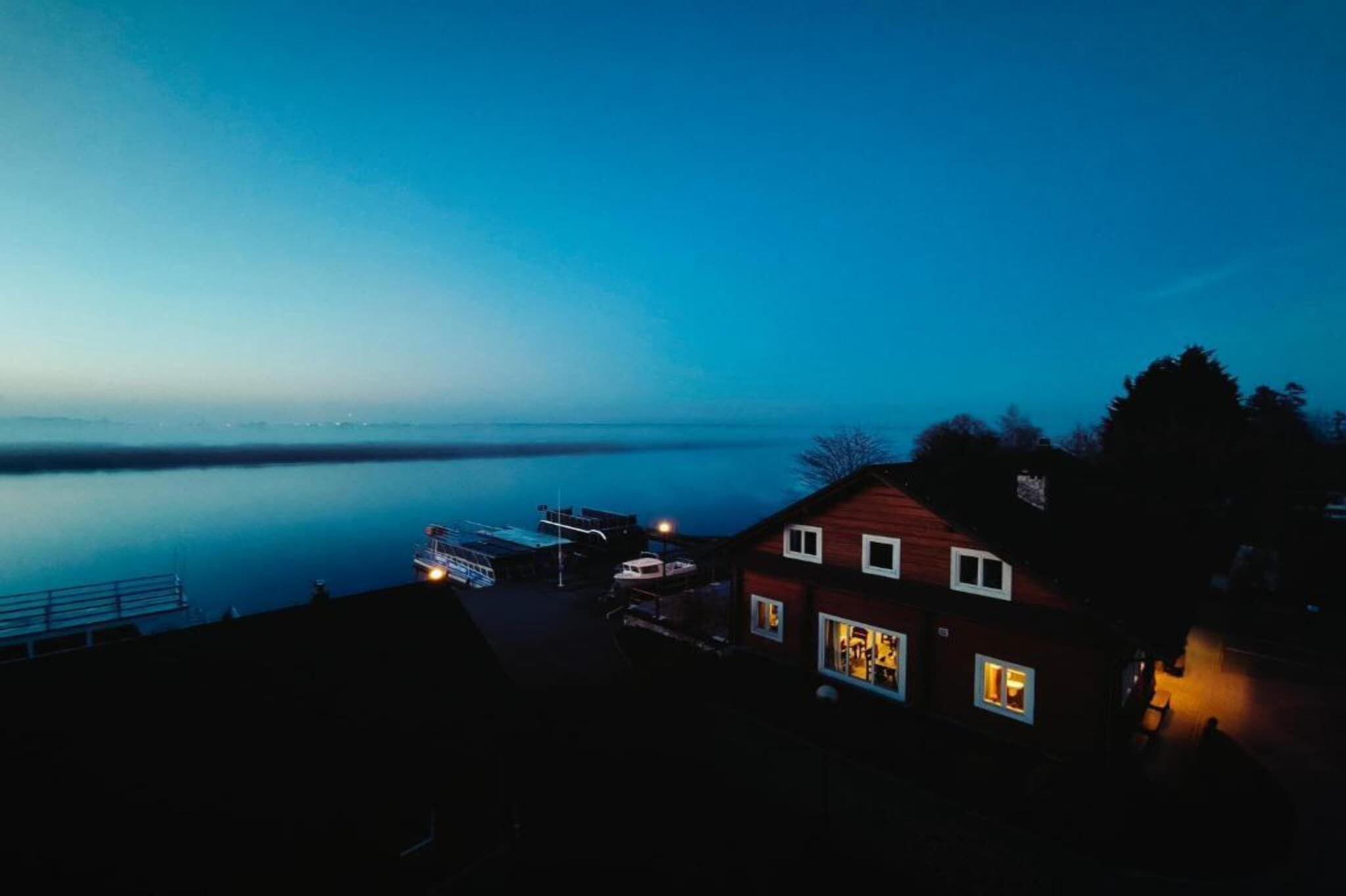 Une maison avec un quai et un bateau, donnant sur une étendue d’eau calme au crépuscule.