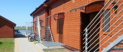 Un edificio de madera con una escalera que conduce a una puerta, una bicicleta estacionada afuera y un cielo despejado.