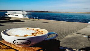 A cup of coffee with latte art on a wooden table by a waterfront. - Double room with breakfast in Świnoujście (Świnoujście)