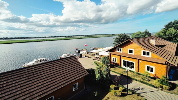 A riverside property with a wooden house, a dock with boats, and a clear view of the river. - Double room with breakfast in Świnoujście (Świnoujście)