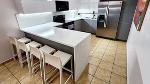A modern kitchen with a central island, bar stools, a microwave, a refrigerator, and a pendant light. - Aquatika Rent beach resort (Vieques)