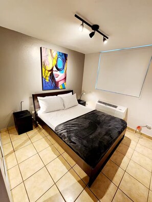 Een slaapkamer met een bed, nachtkastje, radiator en een schilderij aan de muur.