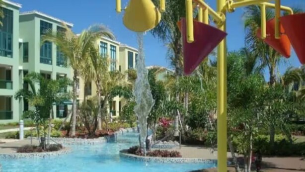 A swimming pool with a water feature, surrounded by palm trees and a building with multiple windows. - Aquatika Rent beach resort (Vieques)