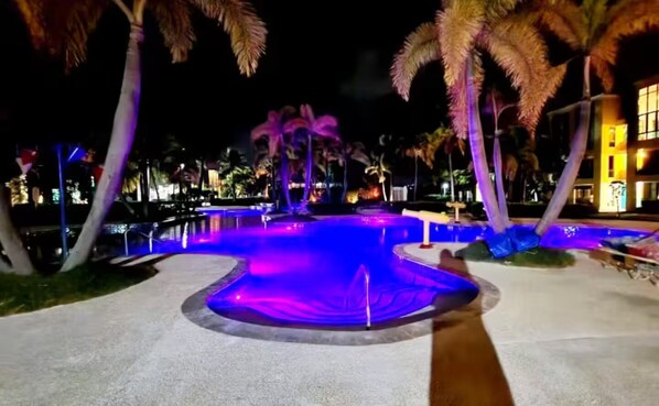 Een nachtzicht van een zwembadgedeelte met verlichte waterornamenten en palmbomen.