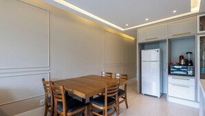 A modern kitchen with a wooden dining table and chairs, a white refrigerator, and a coffee maker.