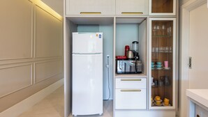 A compact kitchen with a white refrigerator, a coffee maker, and a cabinet with glassware.