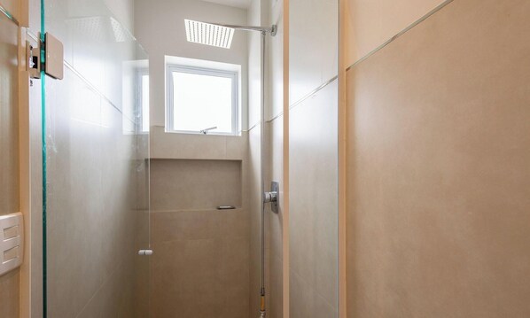 Une douche fermée par des parois en verre, avec une fenêtre au-dessus, une porte et un porte-serviettes.