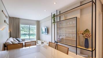 A modern living room with a sofa, a dining table, and a TV mounted on the wall.