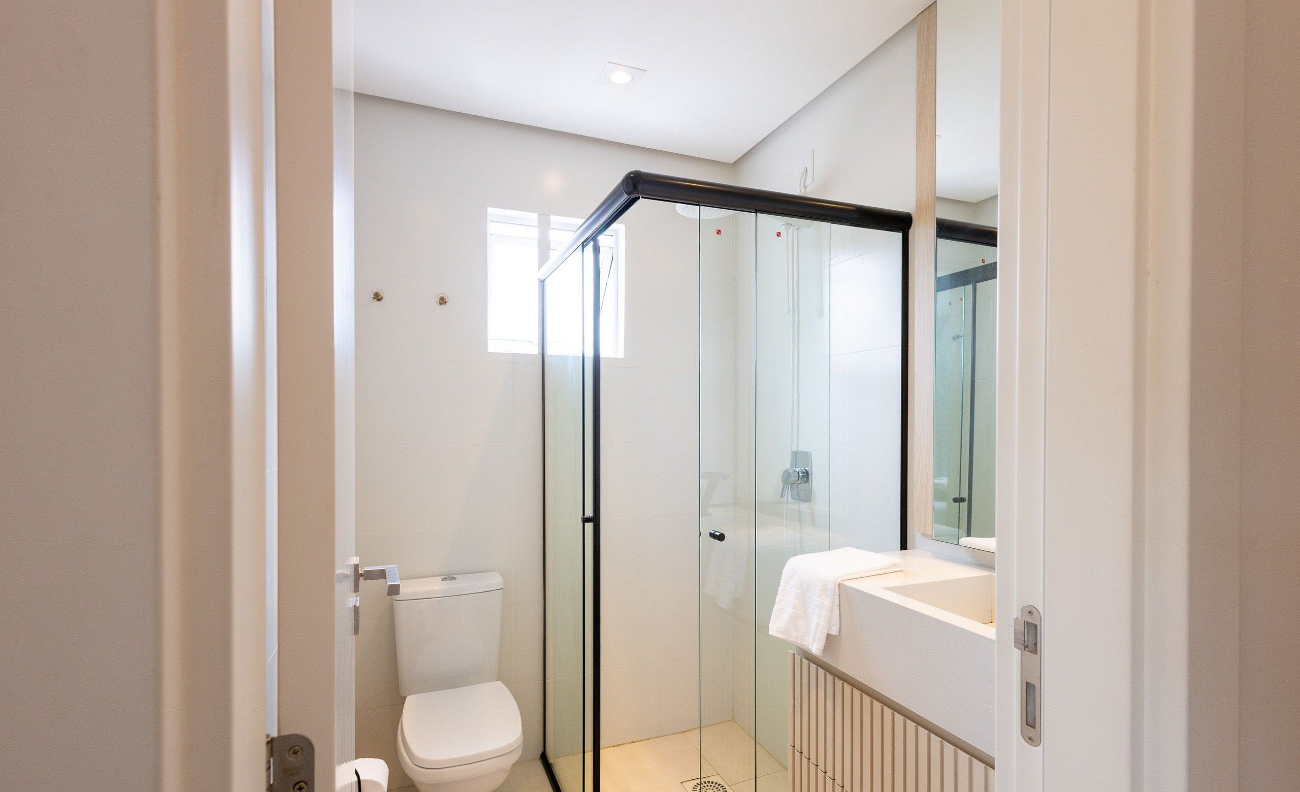 Ein modernes Badezimmer mit Duschkabine aus Glas, Toilette und Waschbecken. Ein Handtuch hängt an der Wand.