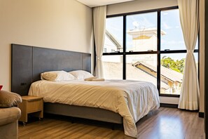 Un dormitorio moderno con una cama grande, una mesita de noche y vistas al exterior a través de amplias ventanas.