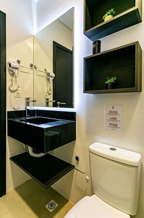 Un baño moderno con un tocador negro, un espejo grande, un inodoro y un estante pequeño con una planta.