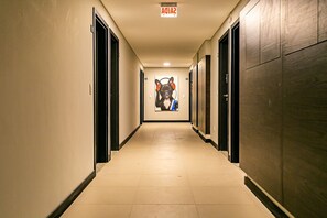 A hotel corridor with doors on both sides, a fire alarm sign at the end, and a poster on the wall.