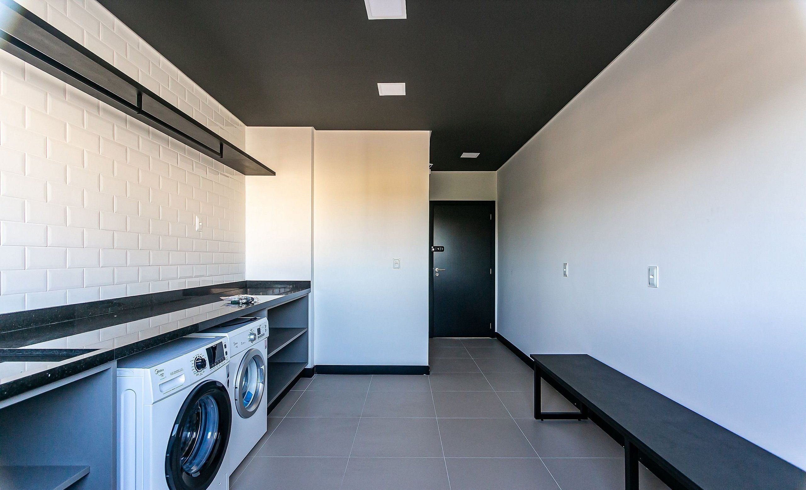 Uma lavanderia moderna com máquina de lavar e secadora, um banco e piso de azulejos.