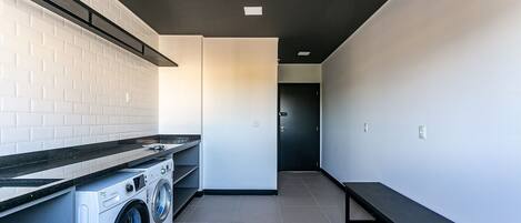 A modern laundry room with a washing machine and dryer, a bench, and a tiled floor.