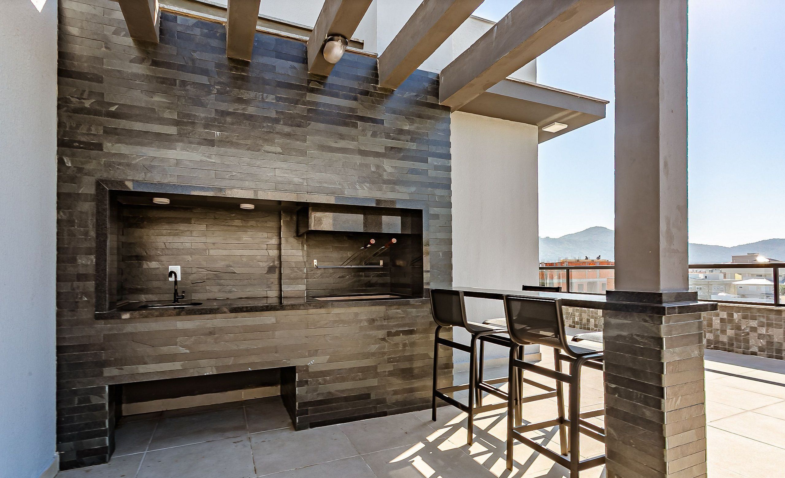 Uma área de cozinha externa com painel de backsplash de pedra, pia e um banco alto.