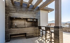 An outdoor kitchen area with a stone backsplash, a sink, and a bar stool. - Modern Studio w/ Family in English Sti105 (Florianópolis)
