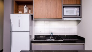 A compact kitchen with a white refrigerator, a microwave, and a sink with a black countertop.