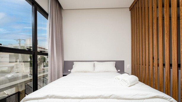 A modern hotel room with a large bed, a wooden headboard, and a view through a large window.