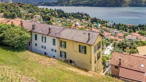 A coastal town with terraced houses, a flag, and mountains in the background. - La Casa Della Seta  (Tremezzo)