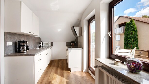 Una cocina compacta con armarios blancos, microondas y cafetera.