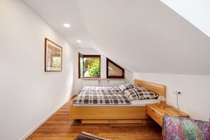 Un dormitorio con una cama de madera, una mesita de noche, una ventana con vista a follaje e iluminación en el techo.