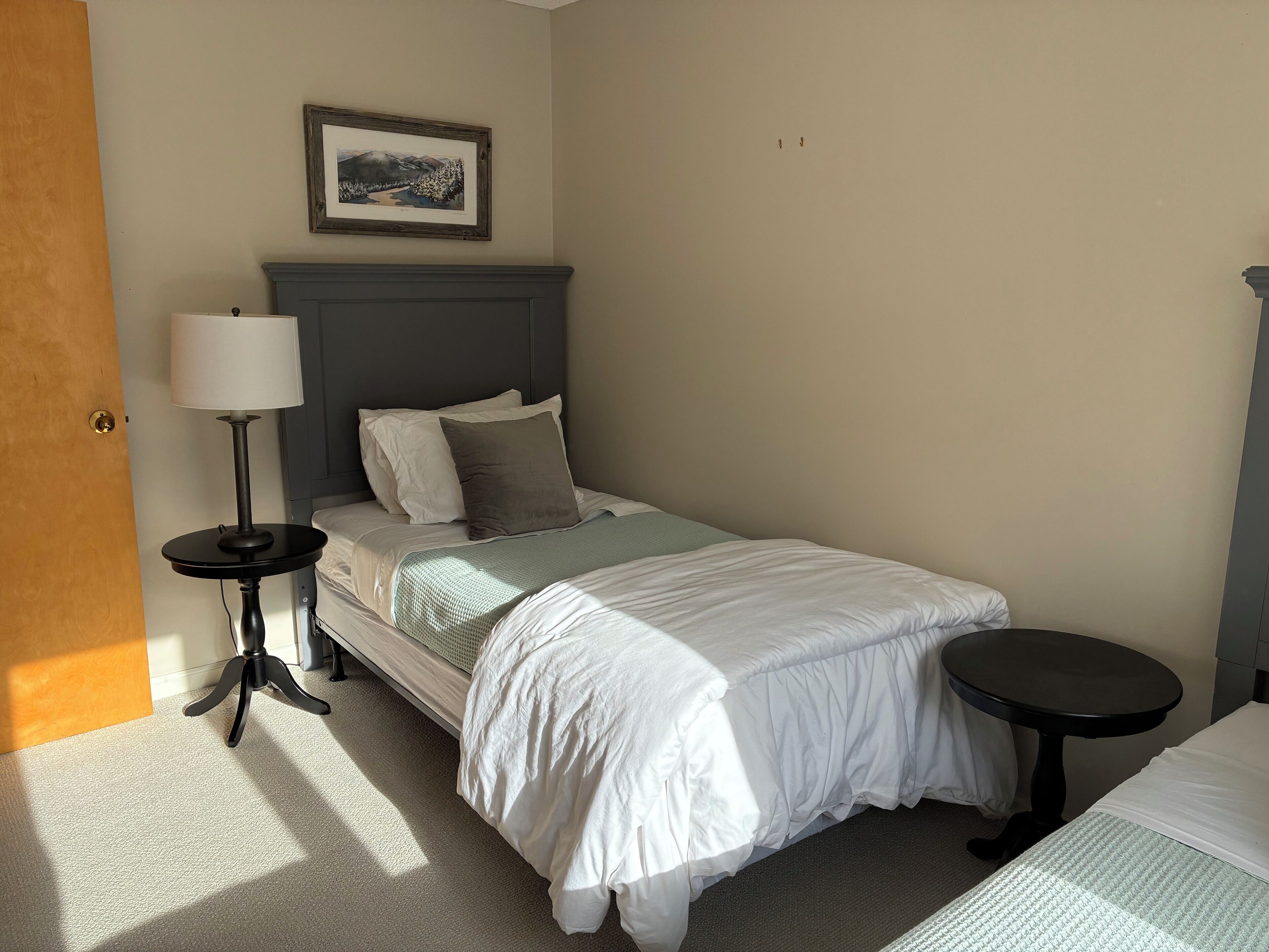 A neatly arranged bedroom with a bed, bedside tables, a lamp, and a framed picture on the wall.