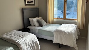 Un dormitorio con dos camas individuales, una mesita de noche, un cuadro enmarcado y una ventana con cortinas.
