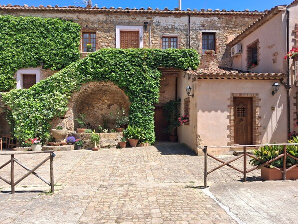 A stone building with a cobblestone courtyard, a wooden gate, and potted plants.
