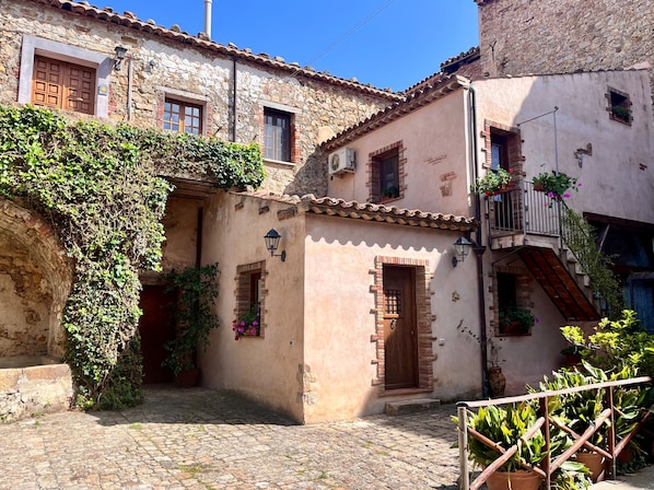 A traditional stone building with a cobblestone courtyard, wooden doors, and potted plants.