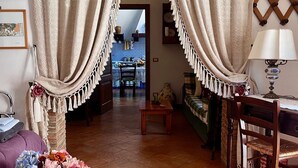 A cozy living room with a wooden floor, a coffee table, and a chair. There is a doorway leading to another room with a blue tiled wall and a dining table. - The Little House in the Courtyard, cozy vacation home with private courtyard in the center (Castelbuono)