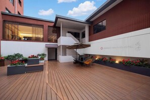 Ein Hotelinnenhof mit einer Holzterrasse, Sitzgelegenheiten im Freien und einer Treppe zu einer oberen Ebene.
