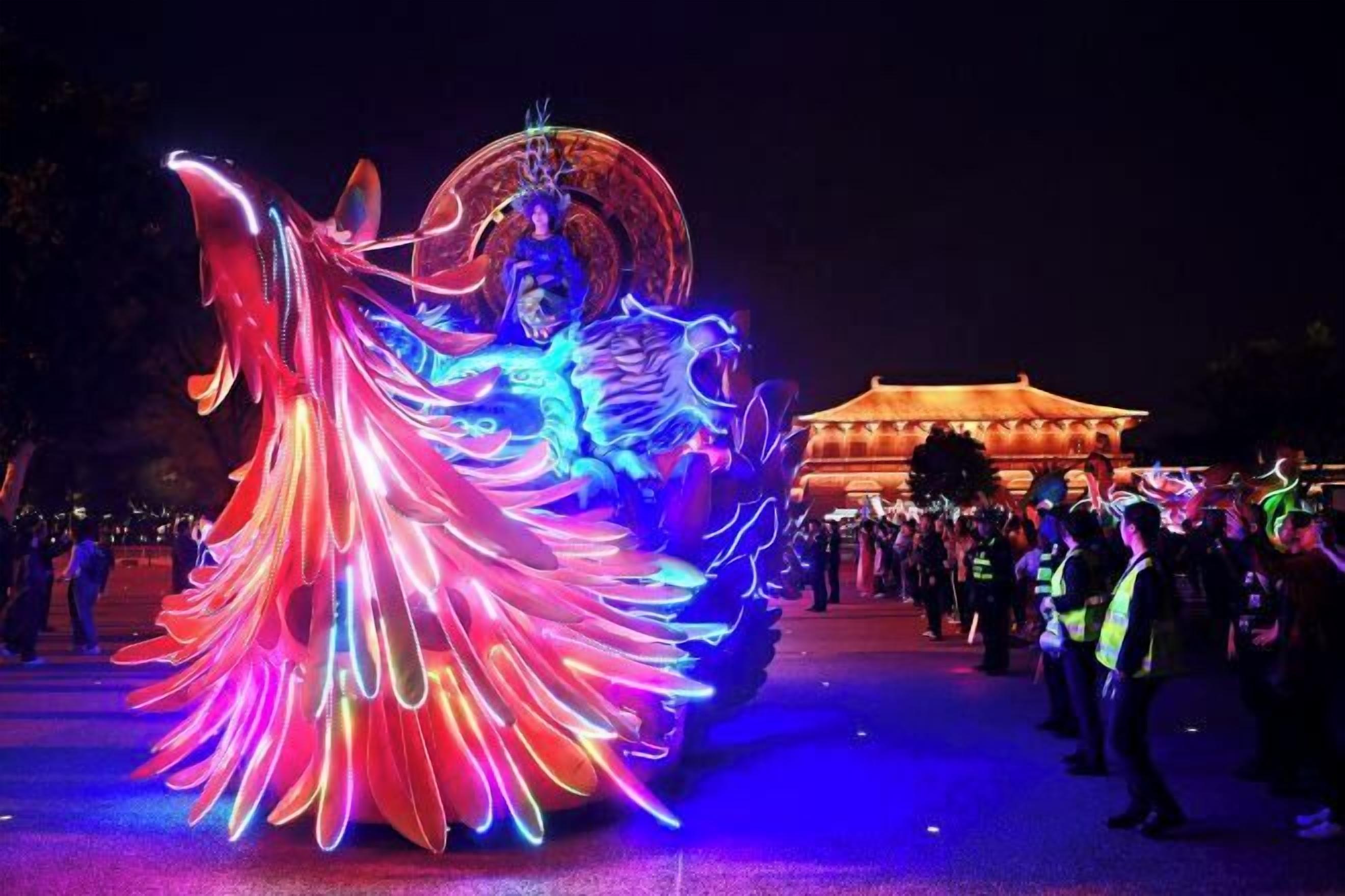 A brightly lit dragon dance performance with traditional architecture in the background.