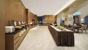 Um hall de hotel moderno com uma mesa de buffet extensa, um balcão de recepção e uma área de estar.