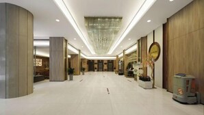 Um hall amplo com um lustre moderno, um balcão de recepção e um quiosque de autoatendimento.