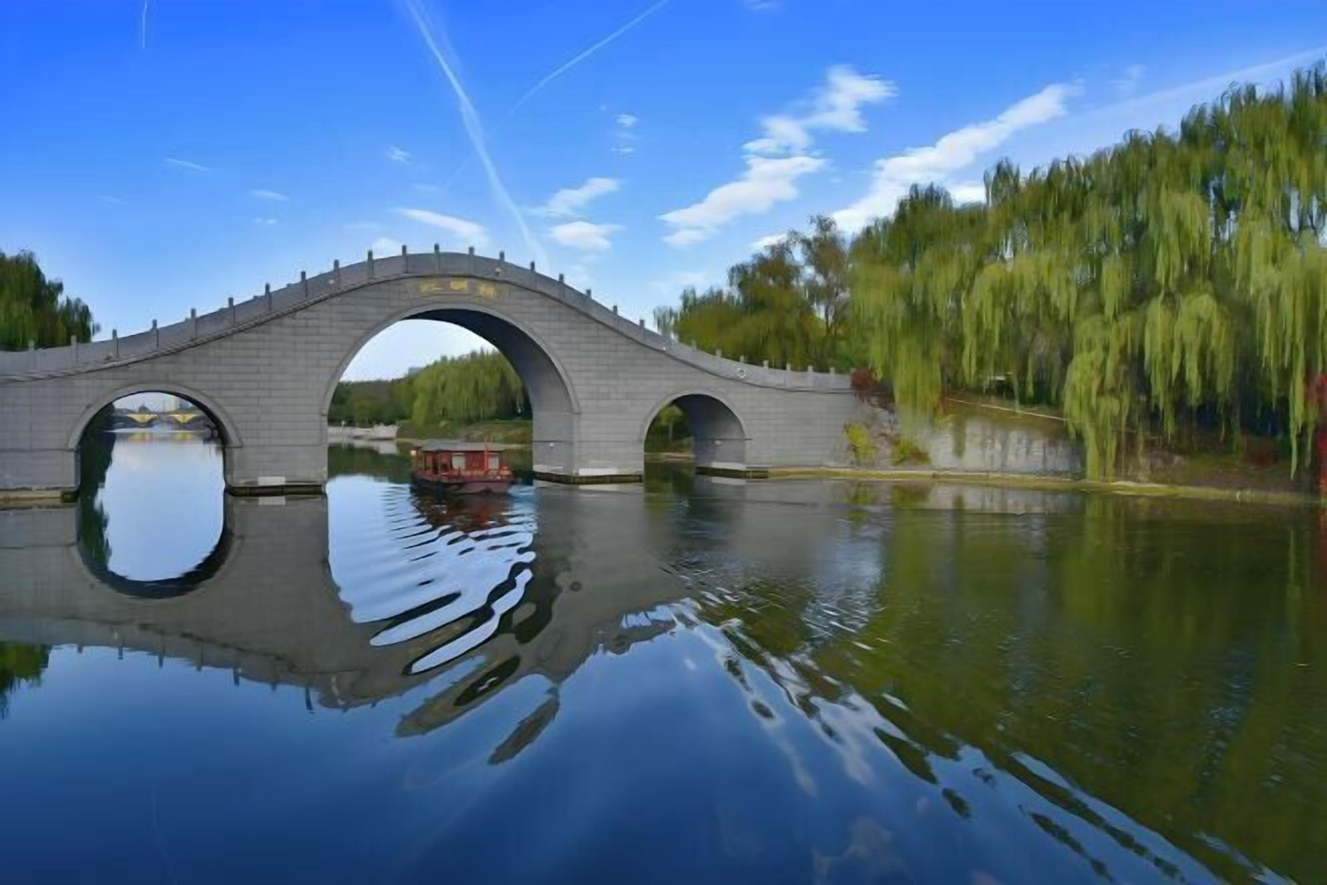 A stone bridge over a calm river with a reflection of the bridge and trees.