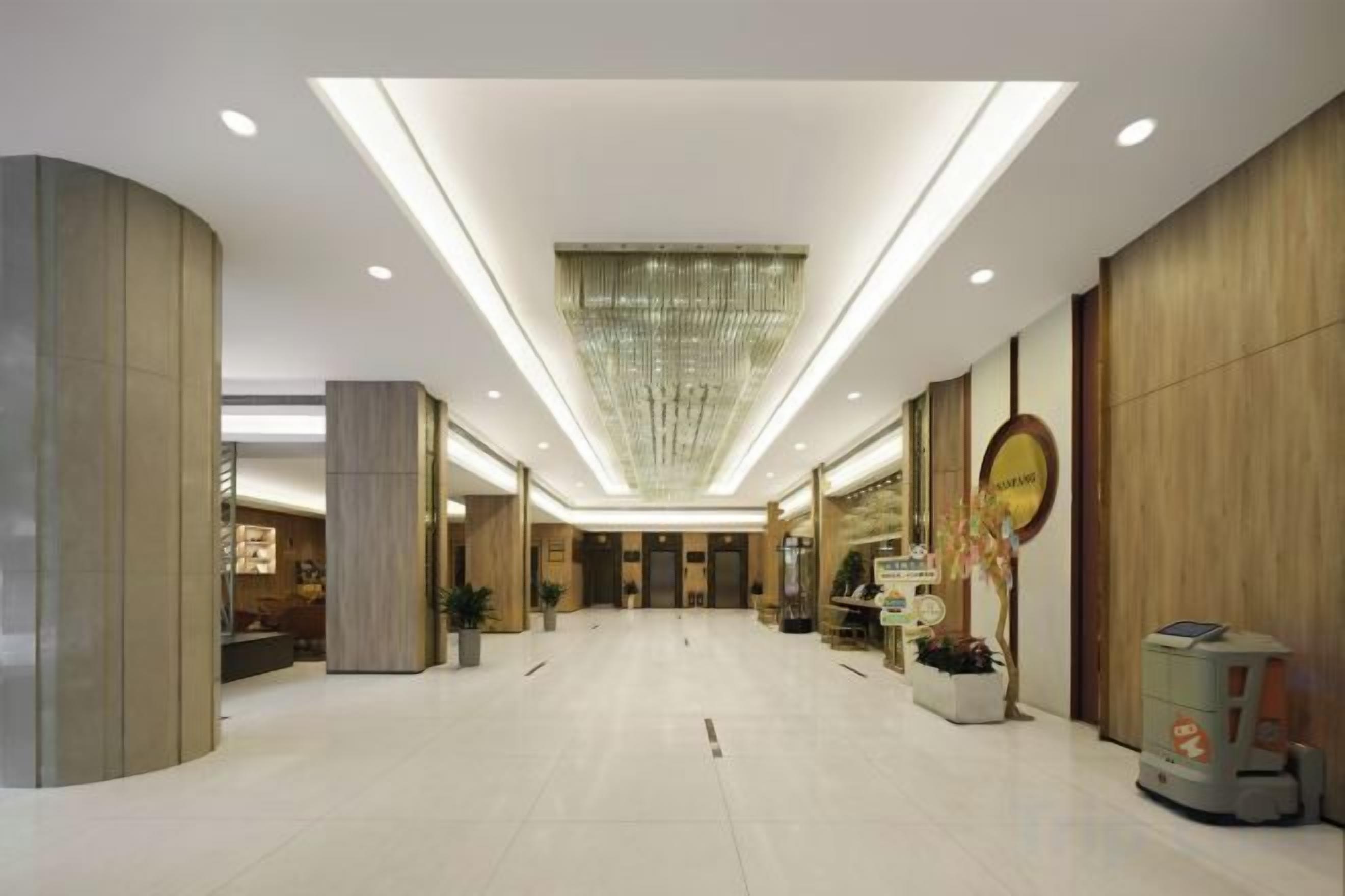 Um hall amplo com teto alto, iluminação embutida e um lustre central.