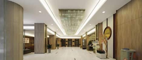 A spacious lobby with a high ceiling, recessed lighting, and a central chandelier.