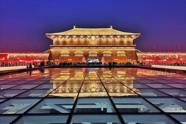 A large, traditional building with a symmetrical facade and a central entrance, surrounded by a reflective water surface.