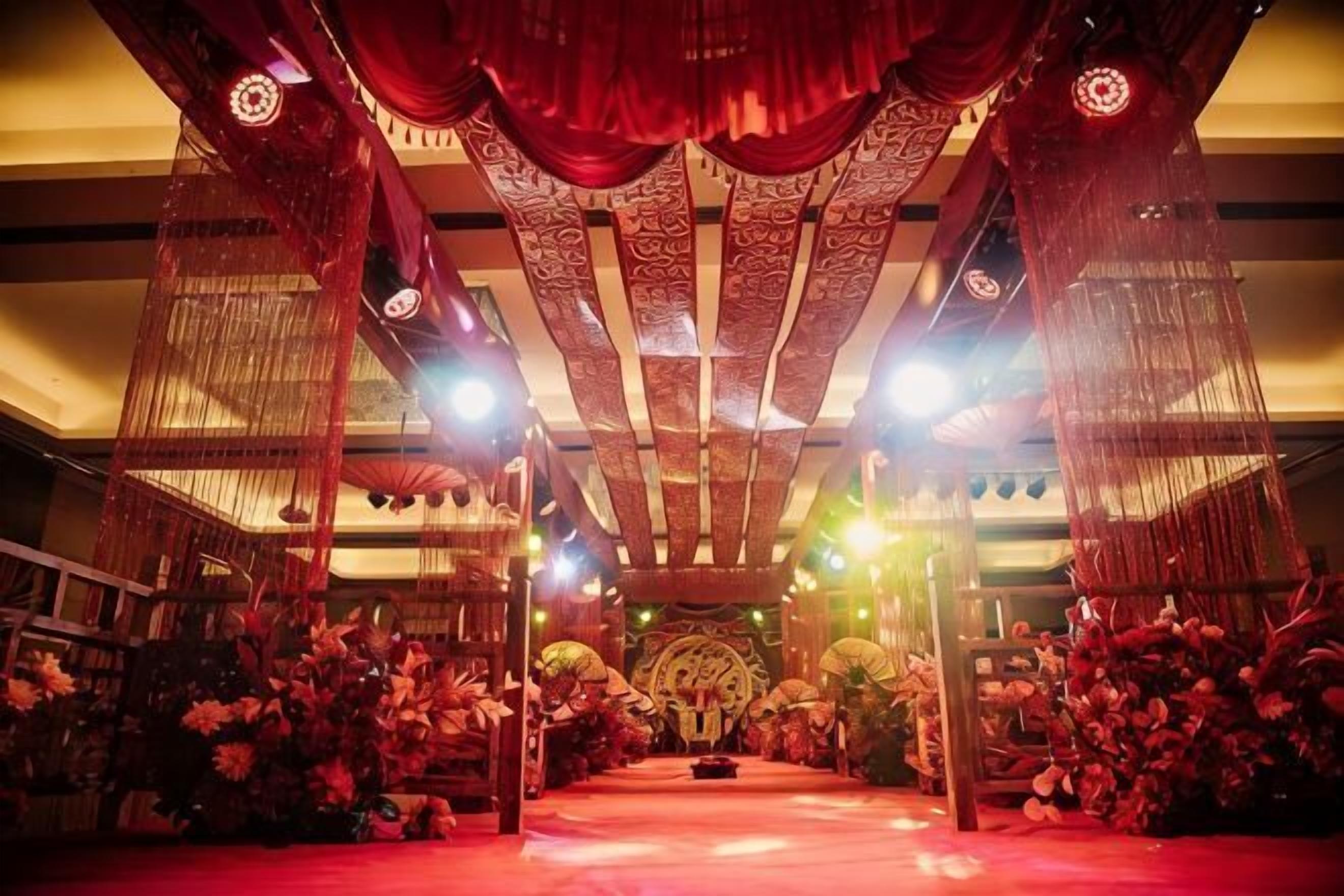An indoor setting with a stage, chairs, and floral arrangements.