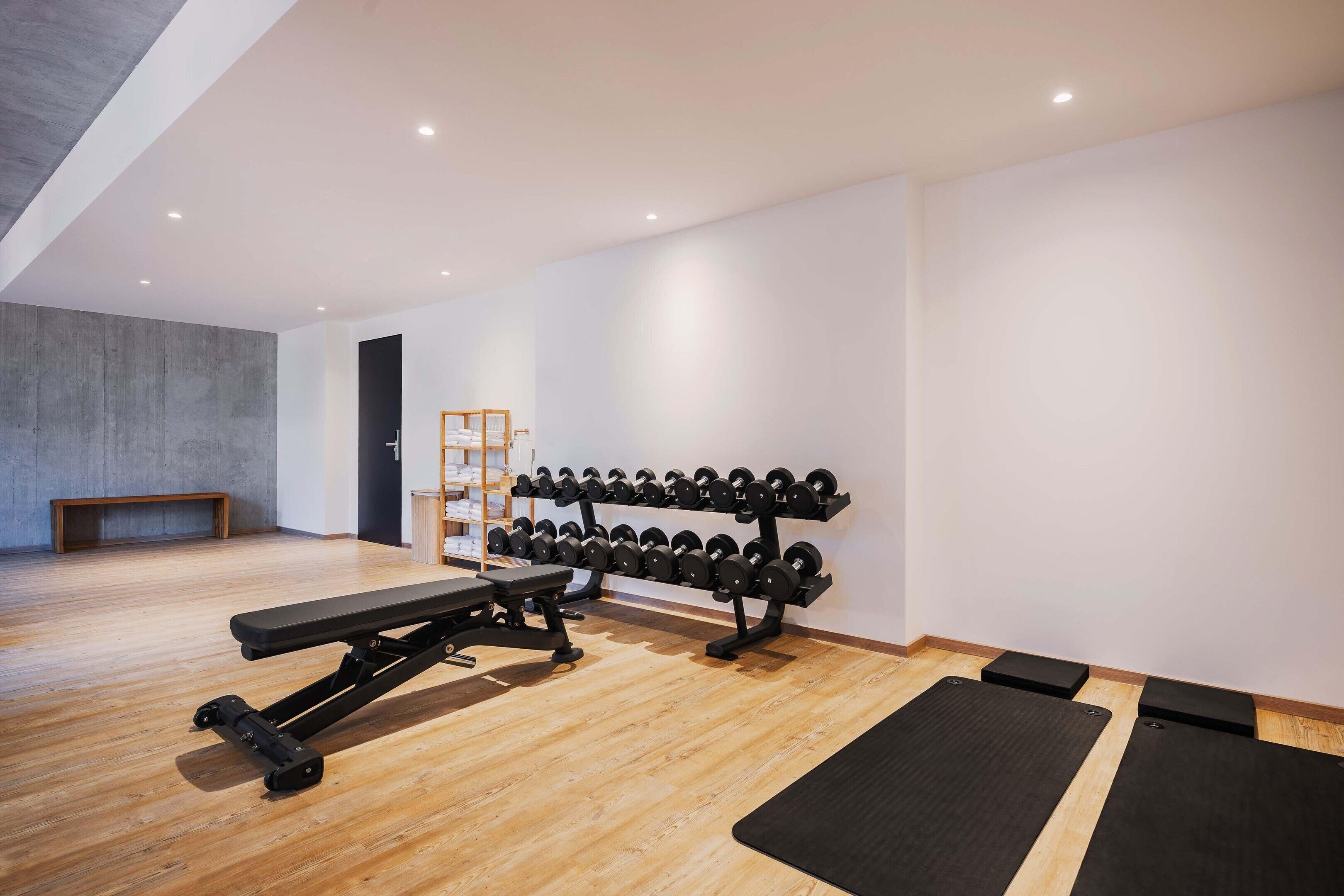 Une salle de sport équipée d’un banc de développé couché, d’haltères et d’un plancher en bois.