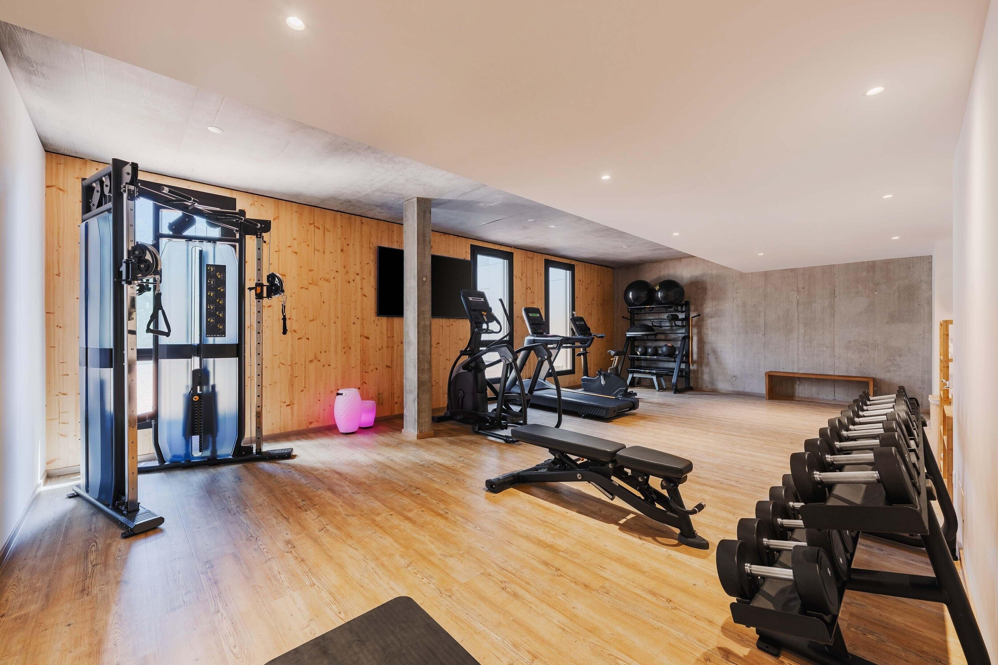 A gym with exercise equipment, wooden walls, and a concrete ceiling.