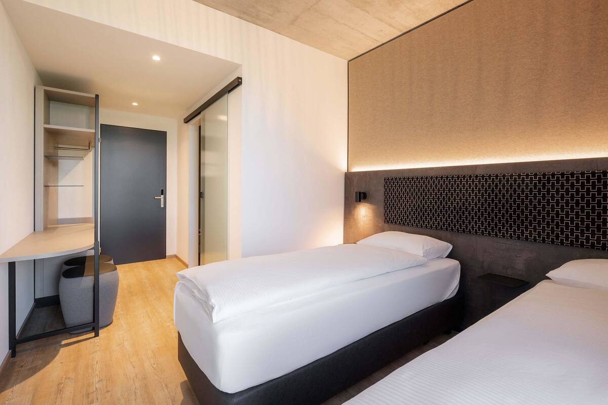 Ein modernes Hotelzimmer mit zwei Einzelbetten, einem Schreibtisch und einem Kleiderschrank.