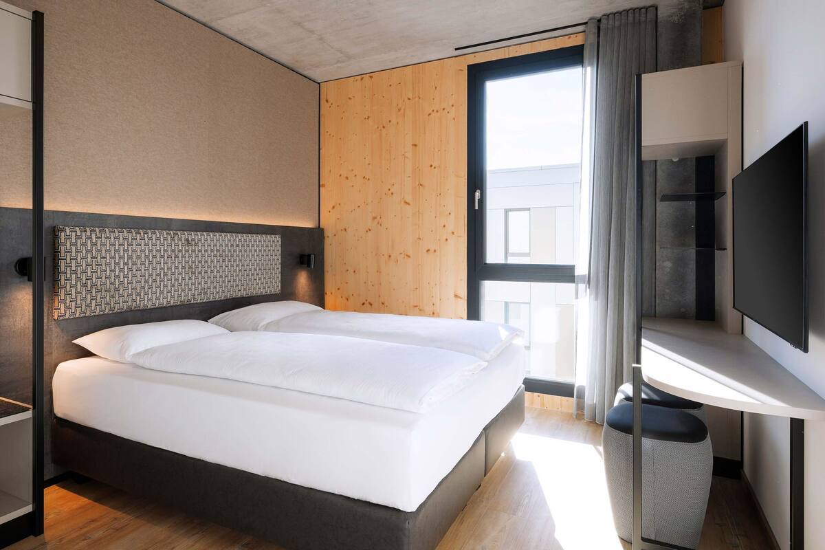 Ein modernes Hotelzimmer mit einem großen Bett, einem Fernseher und einer Wand mit Holzvertäfelung.