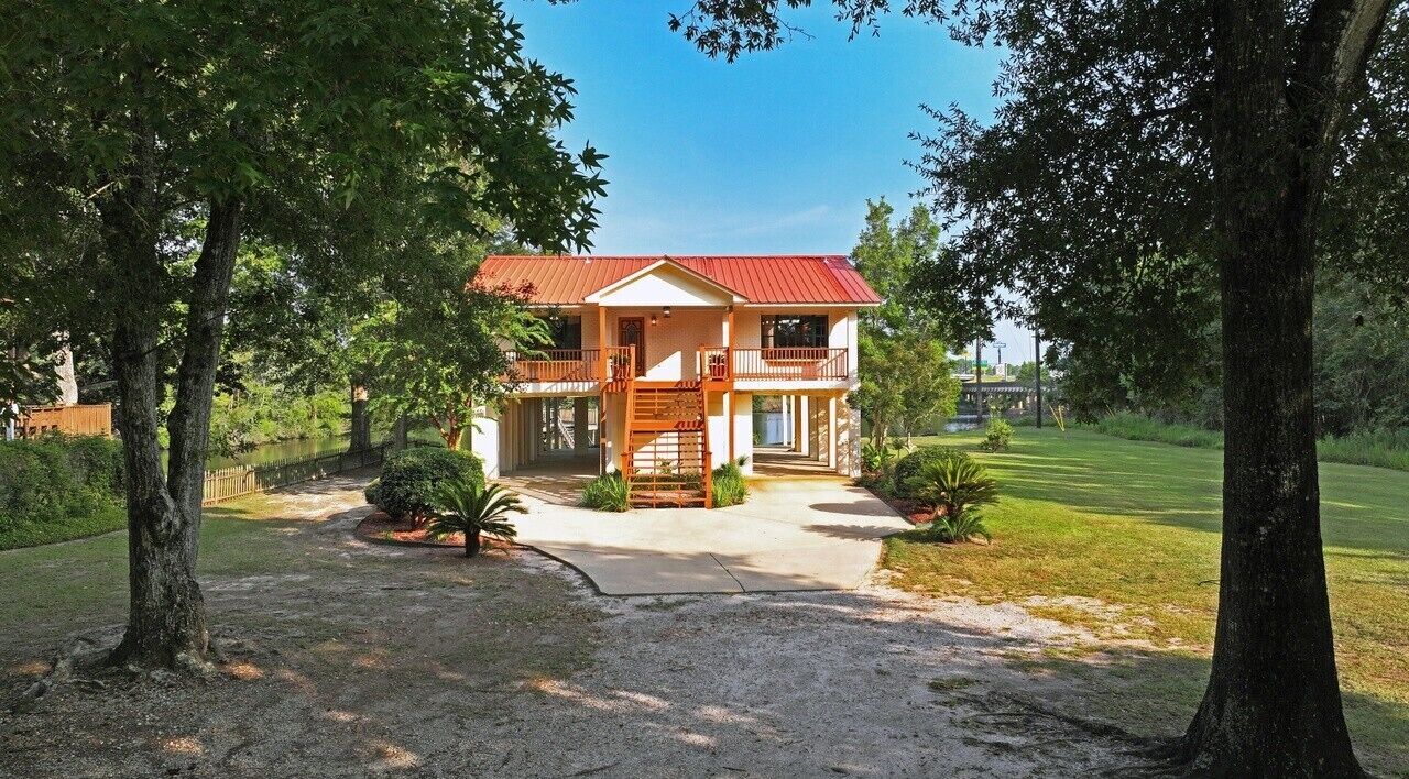 A two-story house with a red roof, surrounded by trees and a well-maintained lawn.
