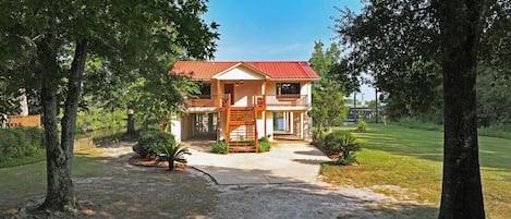 A two-story house with a red roof, surrounded by trees and a well-maintained lawn.