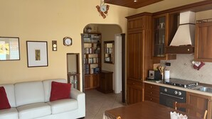 A living room with a white sofa, a wooden dining table, and a kitchen area with wooden cabinets and a stove. - Apartment 'Teresa Al Mare' with Balcony, Wi-Fi and Air Conditioning (Montesilvano)